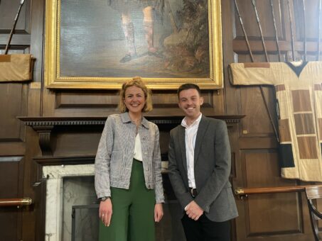 AS man and a woman standing in front of a wood panelled wall and a painting